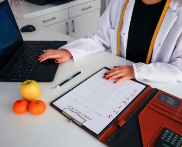 Dietitian working on meal plan with laptop, fruits, and calendar for health consultation.