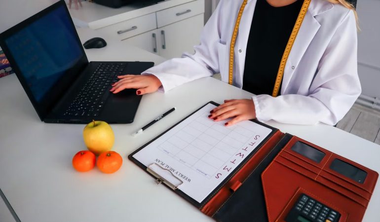 Dietitian working on meal plan with laptop, fruits, and calendar for health consultation.