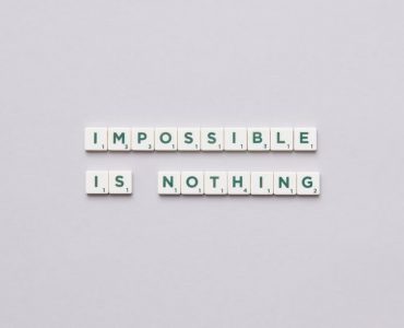Flat lay of Scrabble tiles spelling 'Impossible is Nothing' on a neutral background.