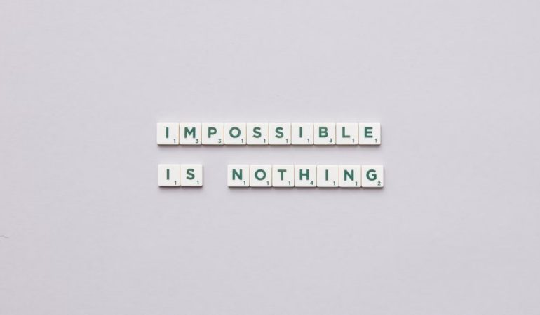 Flat lay of Scrabble tiles spelling 'Impossible is Nothing' on a neutral background.